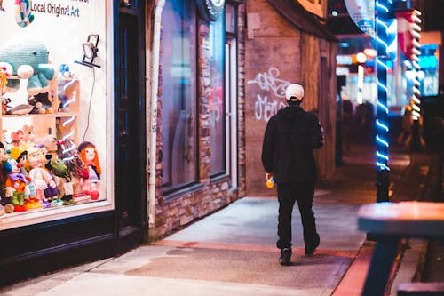 Man walking on sidewalk near illuminated showcases