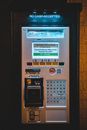 Modern metal machine of parking pay station with keyboard with illuminated display located near wall on street in city in evening time