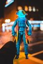 Unrecognizable owner standing on street with glowing astronaut hero in hand with illuminated buildings on blurred background in city in night time