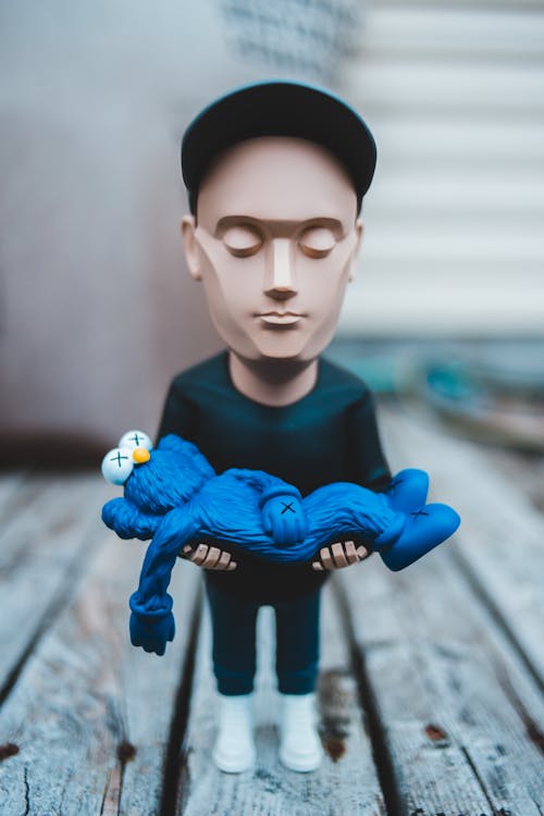Little figurine of man with closed eyes with toy on hands placed on wooden boards on street in city on blurred background