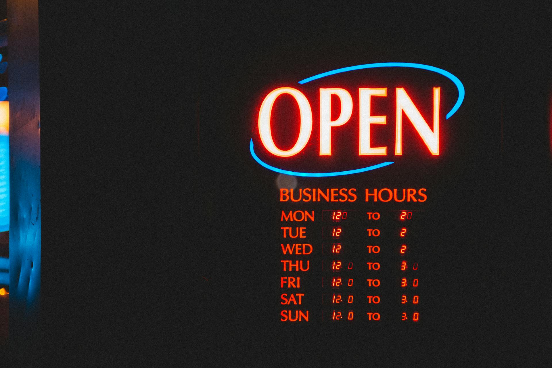 Vibrant neon open sign displaying business hours, captured during nighttime outdoors.