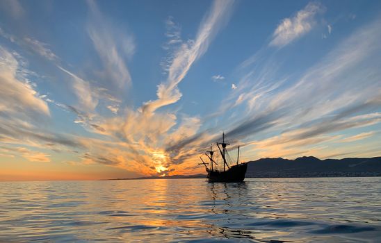 Silhouette of a pirate ship during a breathtaking sunset at sea with stunning sky and reflections.