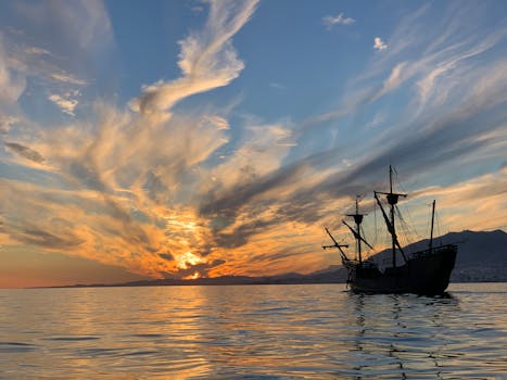 A majestic silhouette of a pirate ship against a vibrant sunset sky with dramatic clouds reflecting on calm ocean waters.