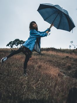 一位身着休闲装的年轻女性神情冷静，在雨天撑着伞，单腿站在草地上