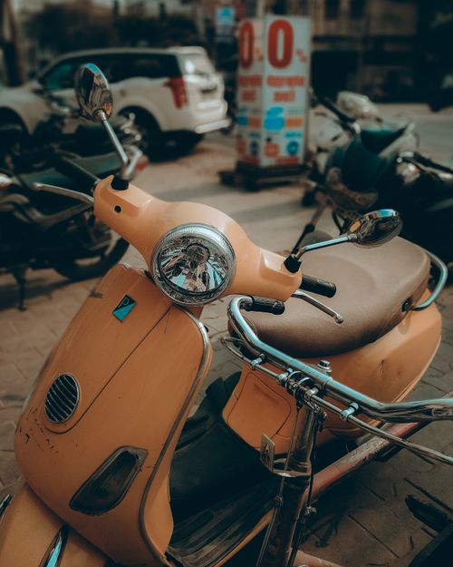 Free Close-up of a vintage yellow scooter parked on a city street with a blurred urban background. Stock Photo