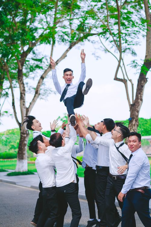 Free A group of young East Asian male graduates celebrating and tossing a friend in the air outdoors. Stock Photo