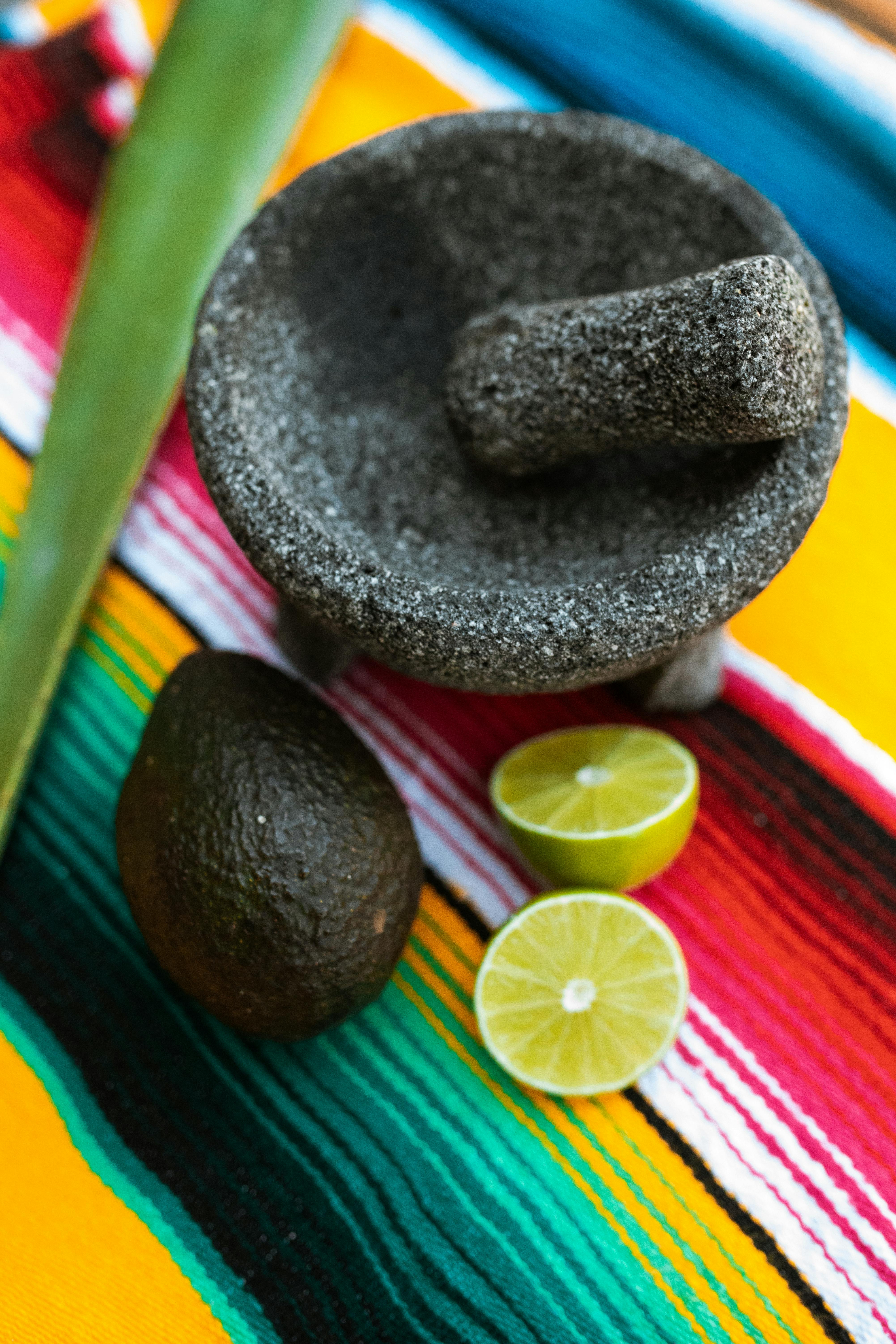 Colorful setup of a molcajete, avocado, and limes on Mexican textile.