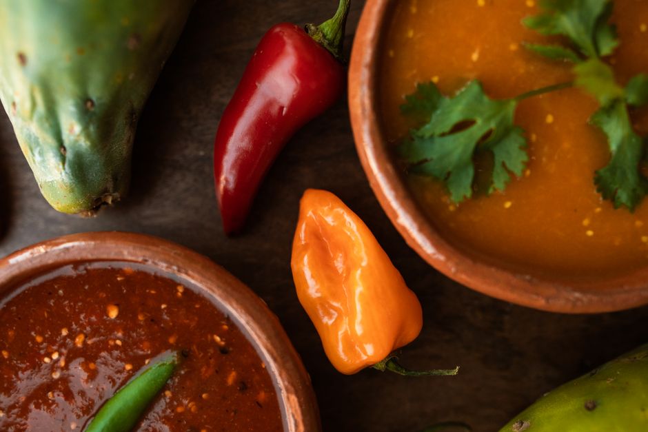 A cluster of small, glossy orange-red wasabinero chili pods still attached to the stem, resting on a wooden cutting board next to a knife.