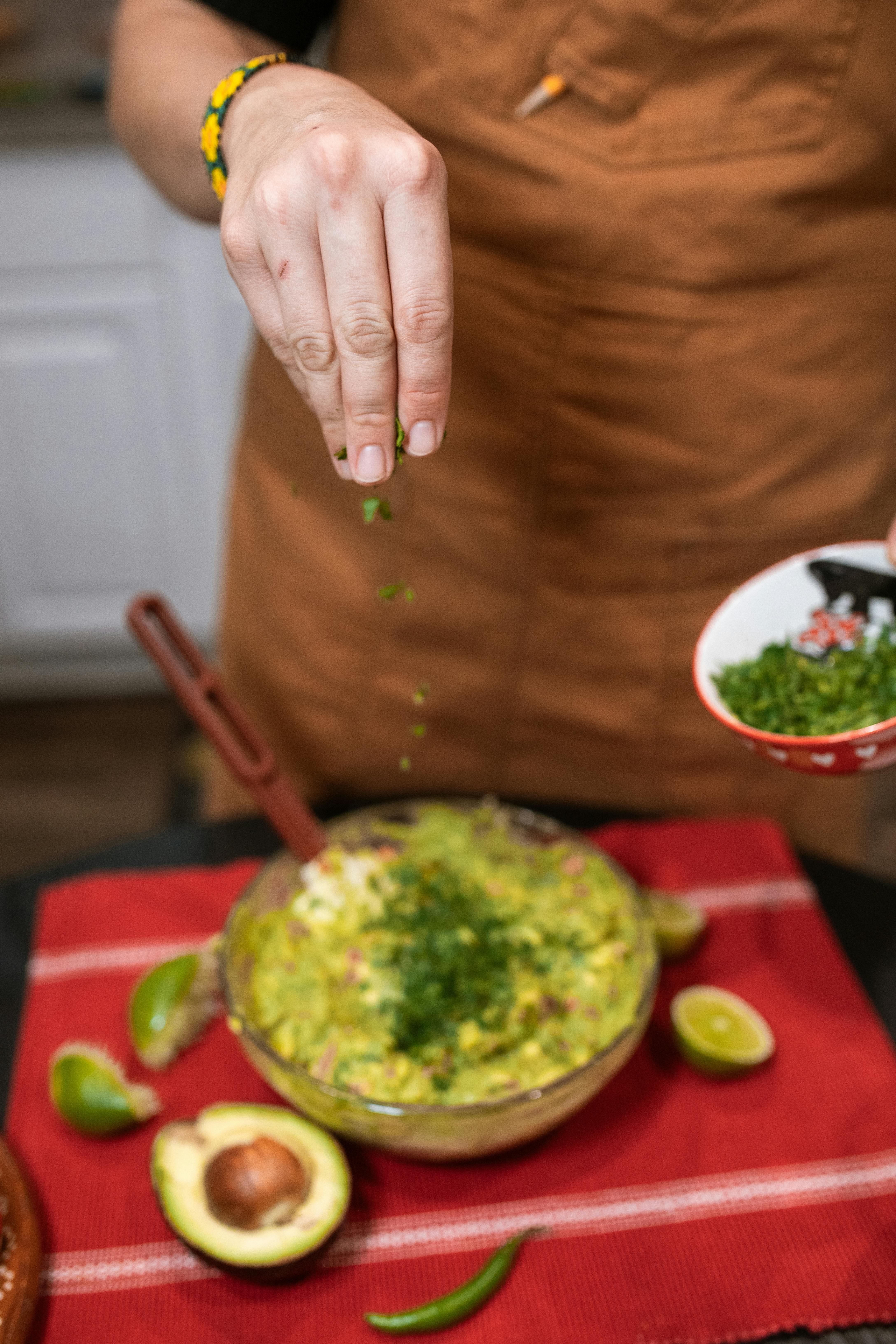 Close-up of a chef adding fresh cilantro to a guacamole bowl with lime and avocado.