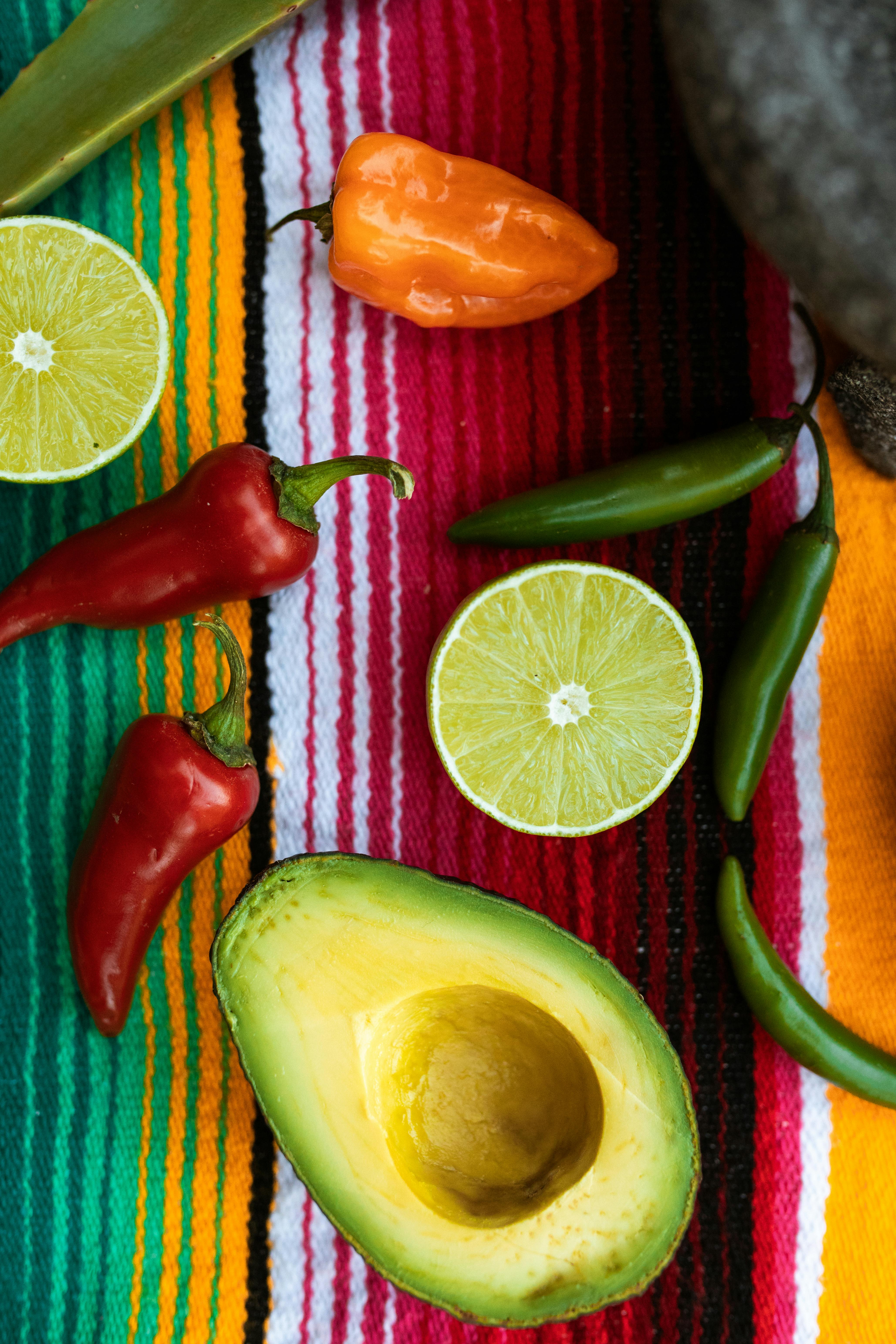 Vibrant still life featuring avocado, peppers, limes on a striped mat. Perfect for culinary themes.