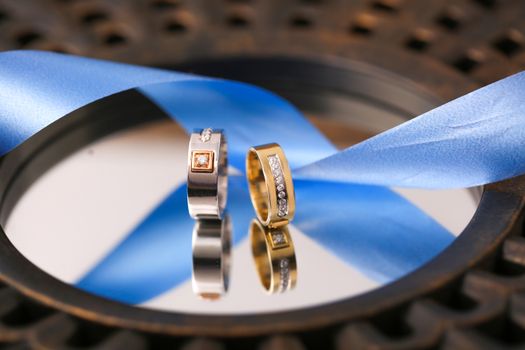 Close-up of two stylish wedding rings on a mirror with a blue ribbon in Surat, India.