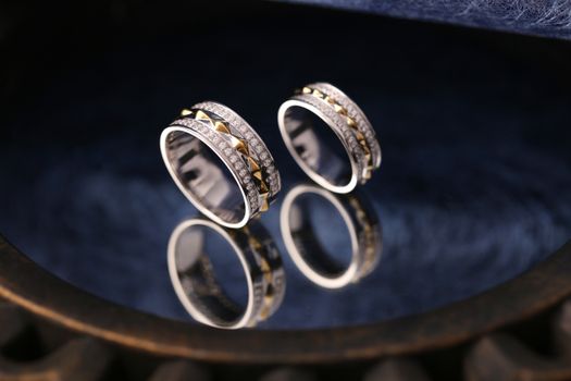 Close-up of elegant silver rings adorned with diamonds reflecting on a dark surface.