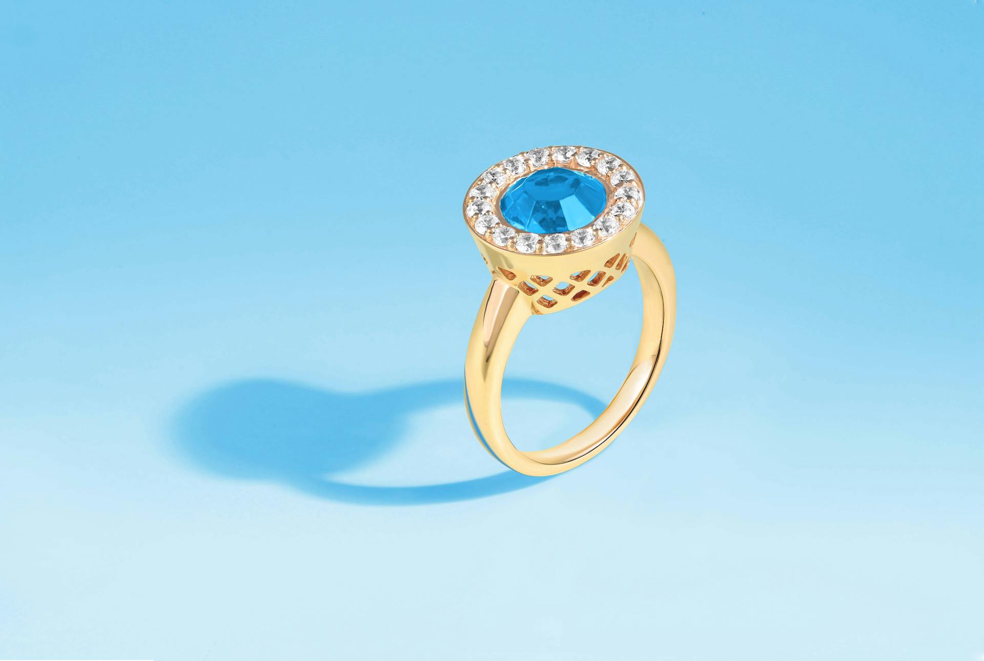 Close-up of an elegant gold ring with a blue gemstone and diamonds on a blue background.