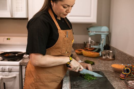 A chef chopping fresh herbs on a cutting board in a modern kitchen setting.