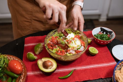 Free Hands preparing fresh guacamole with lime, cilantro, and tomatoes in an indoor kitchen. Stock Photo
