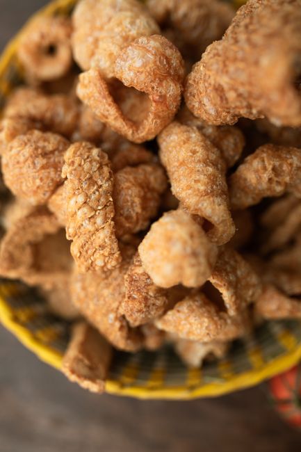 A bowl of golden, puffed pork rinds with visible air pockets, served alongside a small dish of hot sauce.