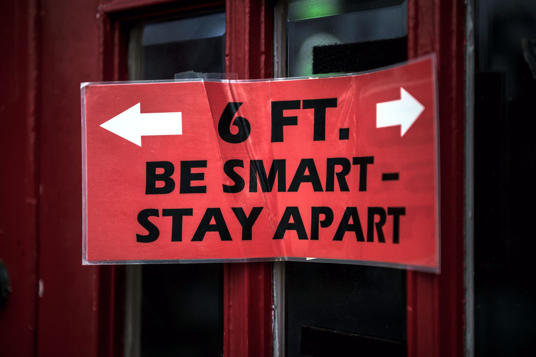Red sign with distancing message: '6 ft. Be Smart - Stay Apart' on a door.