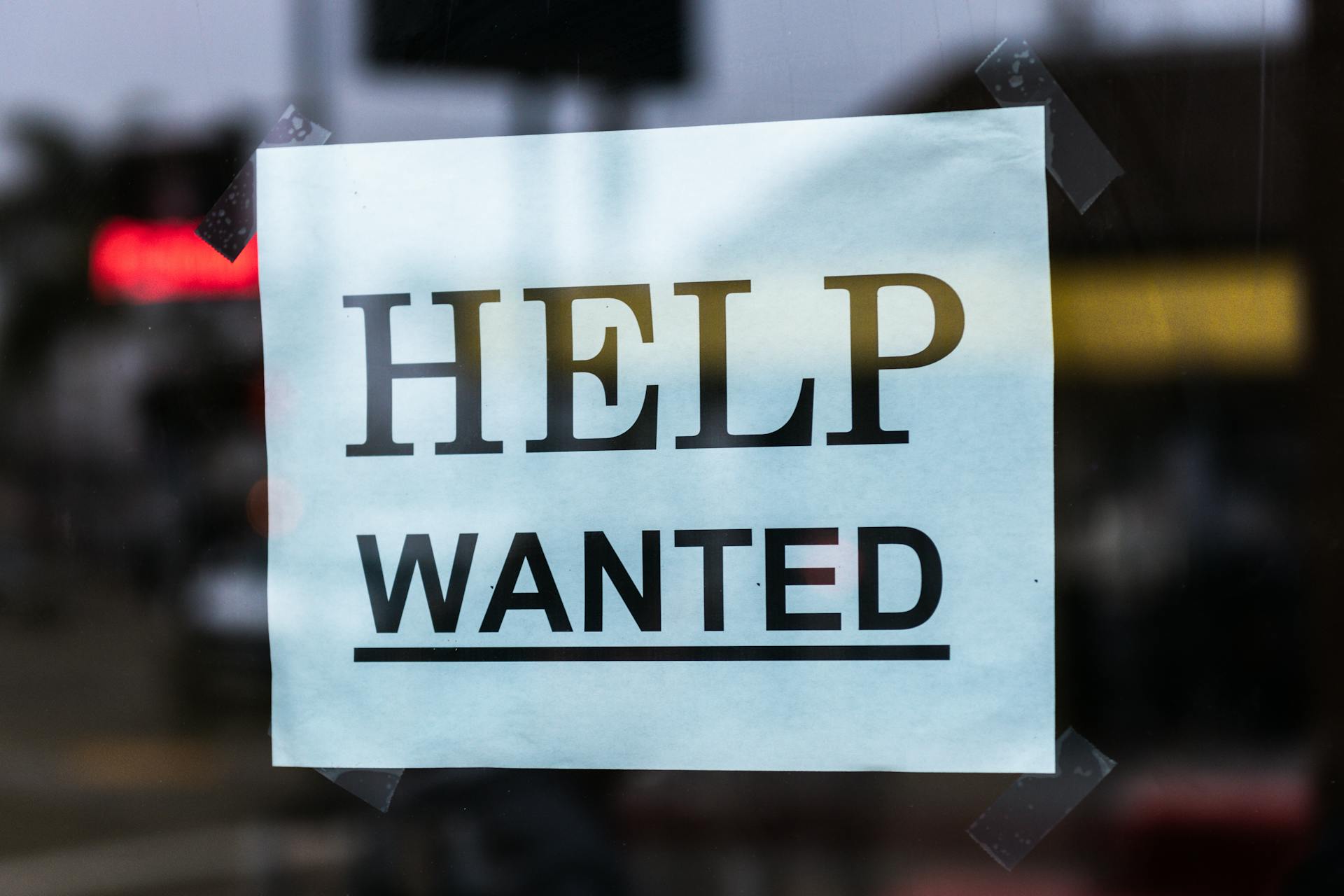 Close-up of a Help Wanted sign taped to a glass window in a storefront.