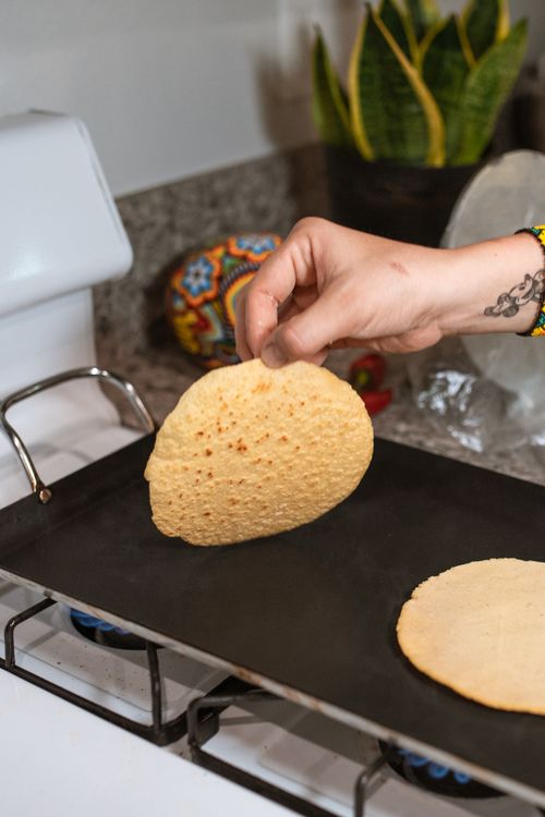 Free Close-up of hand flipping corn tortilla on a griddle, capturing traditional cooking style. Stock Photo