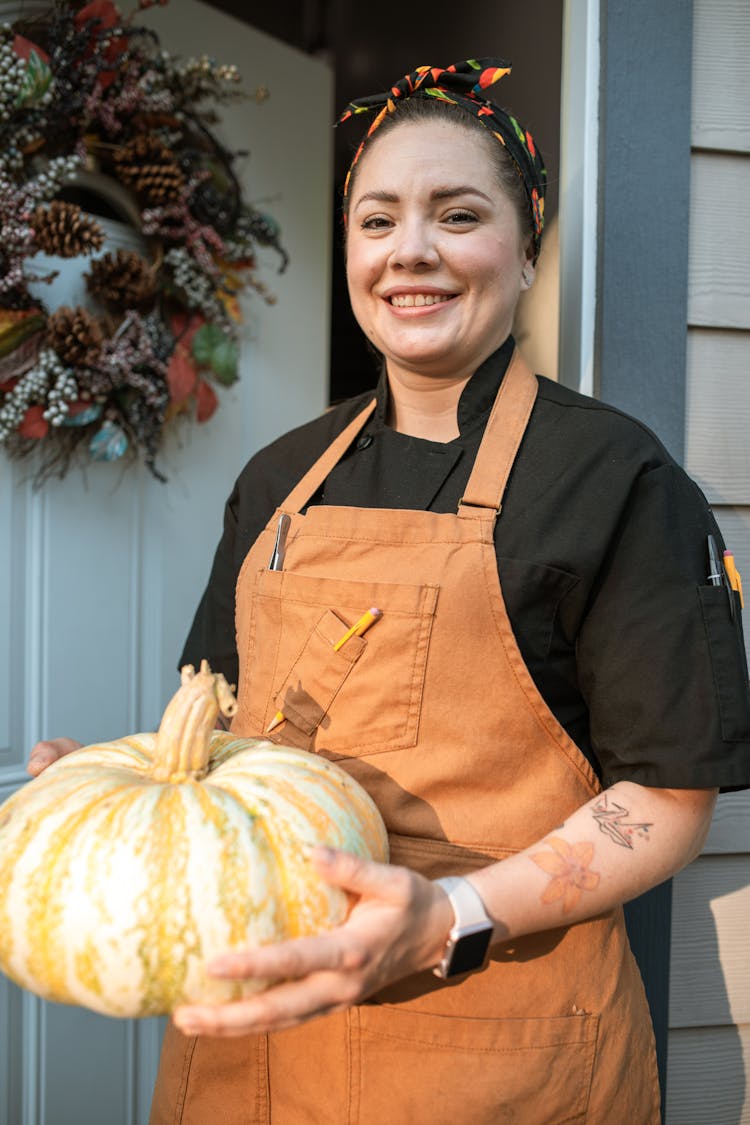 A Smiling Woman In Brown Apron Holding A Pumpkin