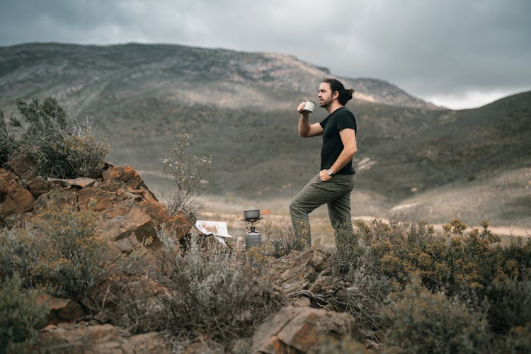 A Man In Black Shirt Standing While Drinking Coffee Near The Mountain