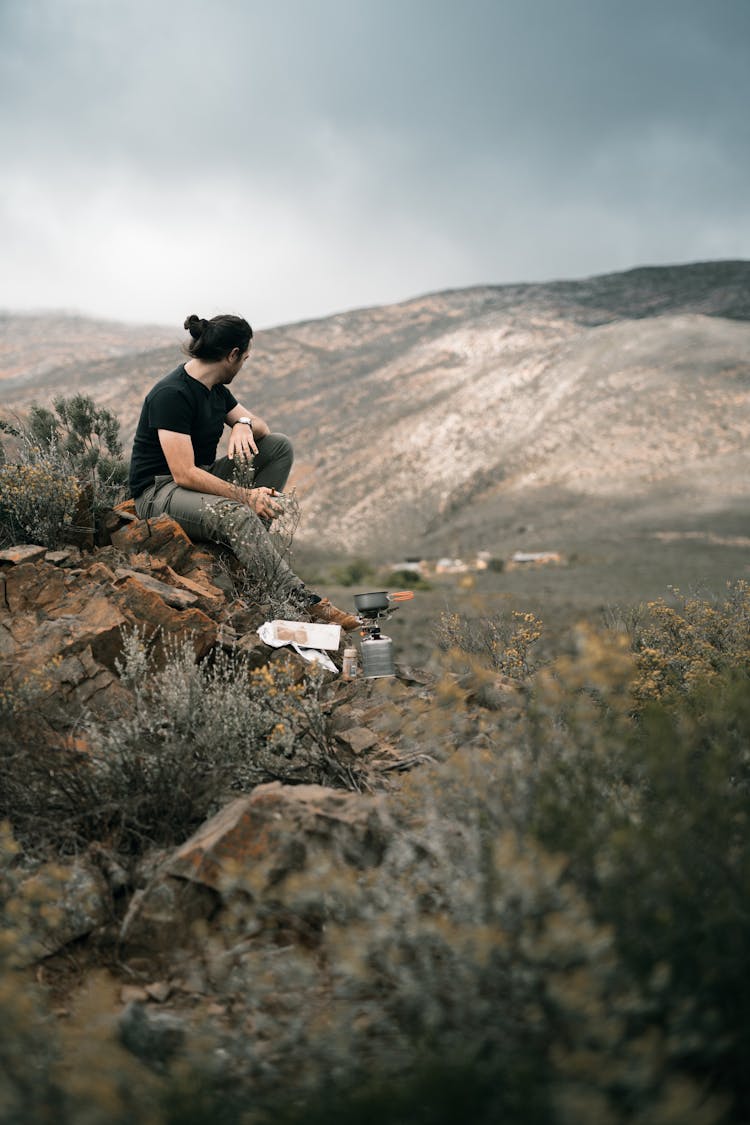 A Man In Black Shirt Sitting On The Rock While Looking At The View