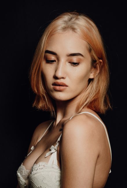 Side view of young tender woman in white bra with blond hair looking down on black background