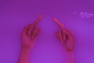 Top view of crop anonymous rude female demonstrating middle fingers in aqua with neon light