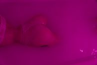 From above back view of crop anonymous seductive female in bra and thong lying in water in neon light
