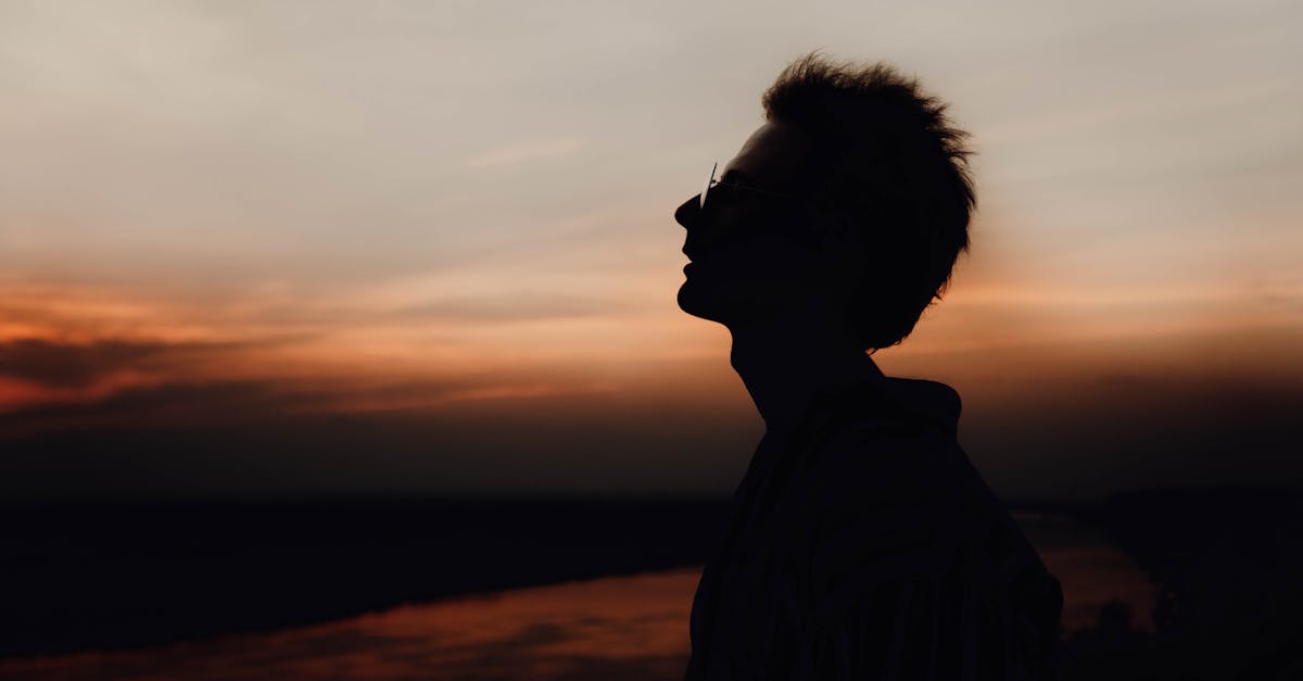 Side view of lonely male silhouette in eyeglasses breathing and admiring cloudy sky at night