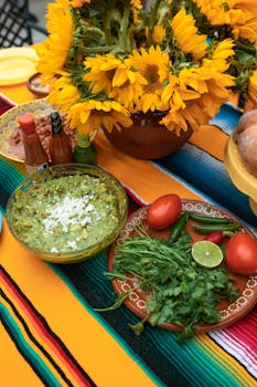 Colorful Mexican feast with fresh guacamole, sunflowers, and vibrant ingredients on a table.