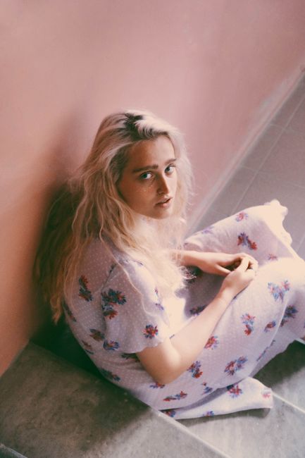 From above side view of young timid female with blond hair looking at camera while sitting on staircase in house