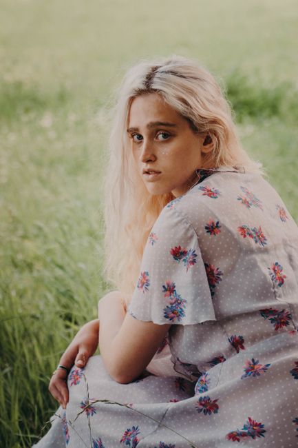 Side view of young tender female in ornamental wear looking at camera while sitting in countryside field