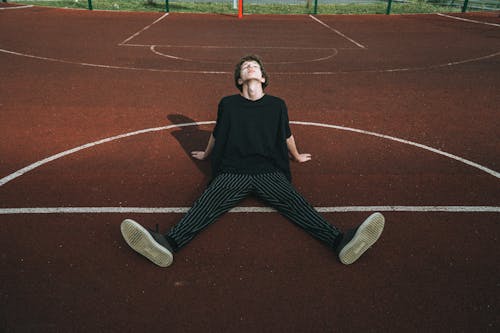 Male teen in striped trousers leaning with hands on recreation ground on sunny day