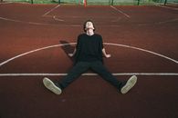 Male teen in striped trousers leaning with hands on recreation ground on sunny day