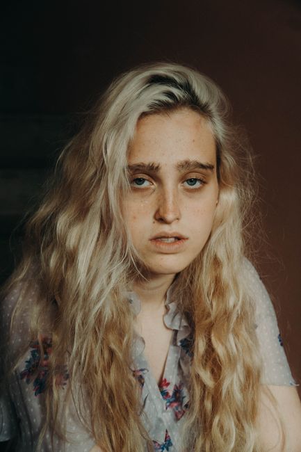Young exhausted female with long wavy hair in apparel with ornament looking at camera