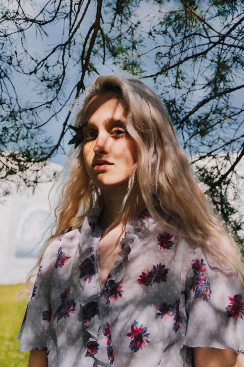 Free Young gentle female in clothes with floral ornament and shade on face looking at camera on lawn Stock Photo
