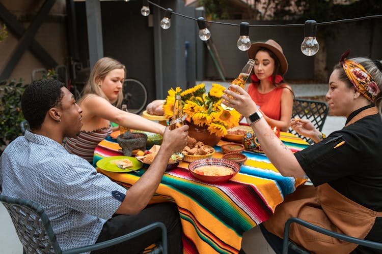 A Man And Woman Toasting Beer Bottles While Sitting Near The Table