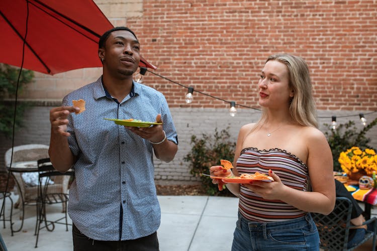 Man And Woman Holding Their Plates While  Eating Nachos