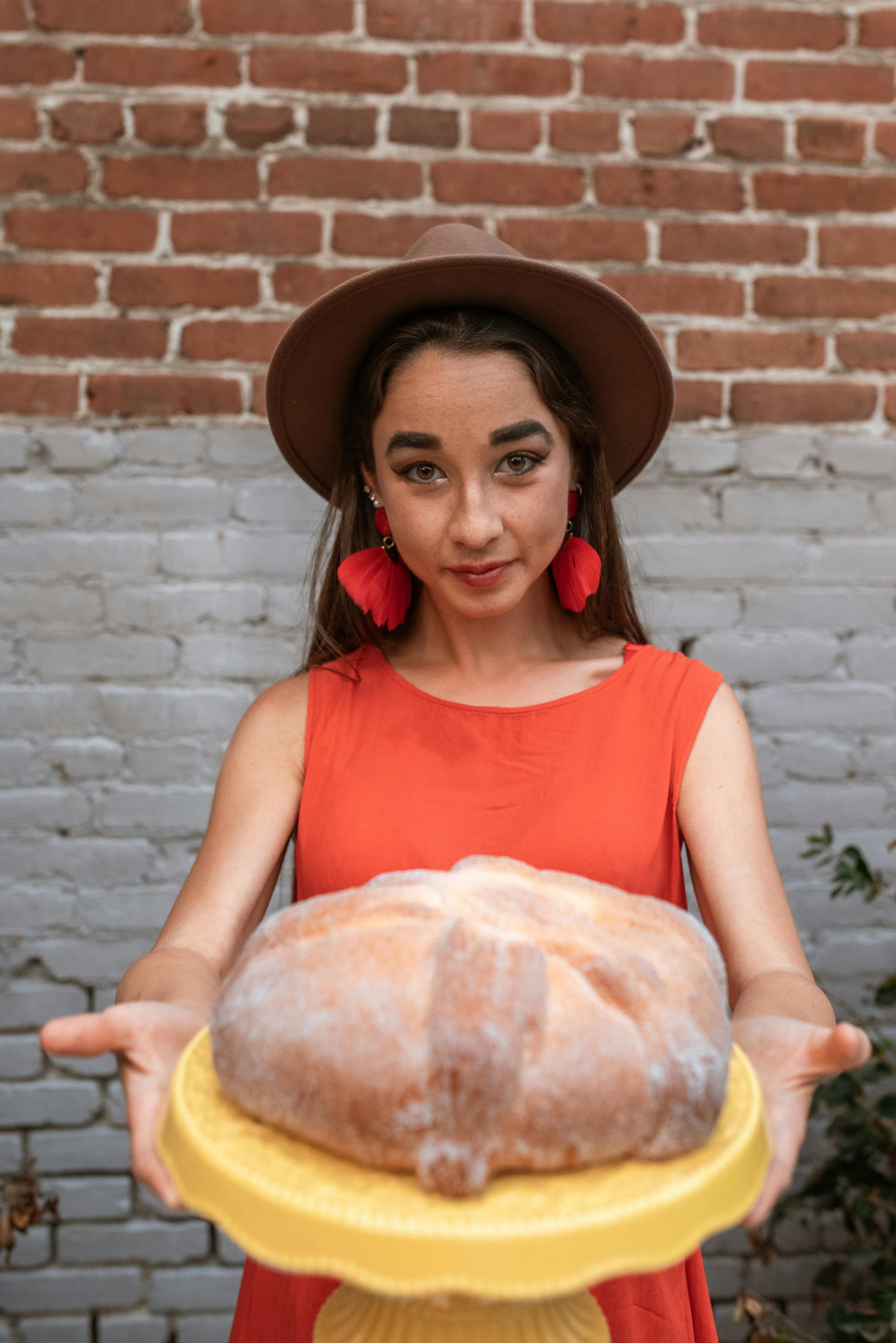 A woman in a hat and earrings presents a freshly baked Pan de Muerto.
