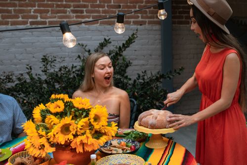 Free Two women enjoying a festive meal outdoors with bread and vibrant sunflowers on the table. Stock Photo
