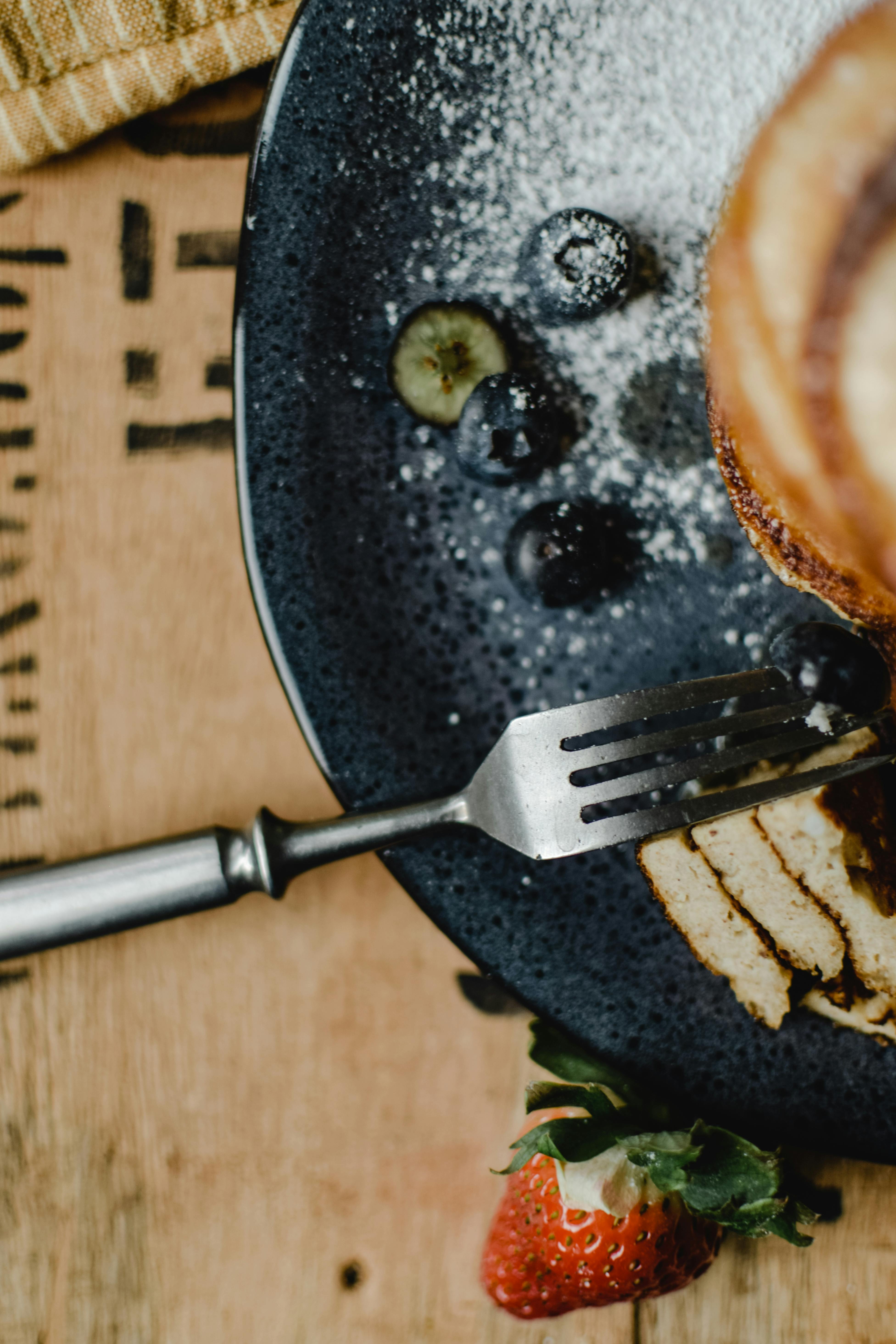 Tasty pancakes topped with berries and powdered sugar on a plate with a fork.