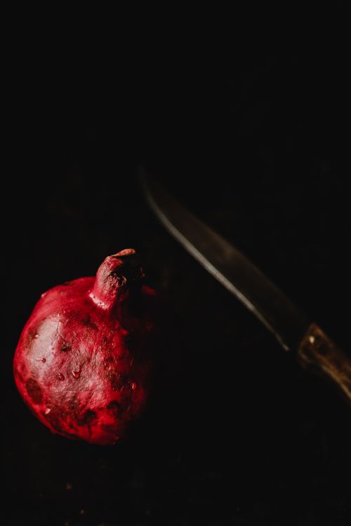 Free A dark, atmospheric shot of a whole pomegranate and knife, highlighting texture and contrast. Stock Photo