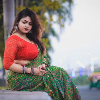 Beautiful woman in colorful saree sitting outdoors. Traditional Indian fashion.