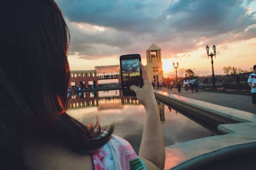 免費 女人抱著智能手機捕捉日落 圖庫相片