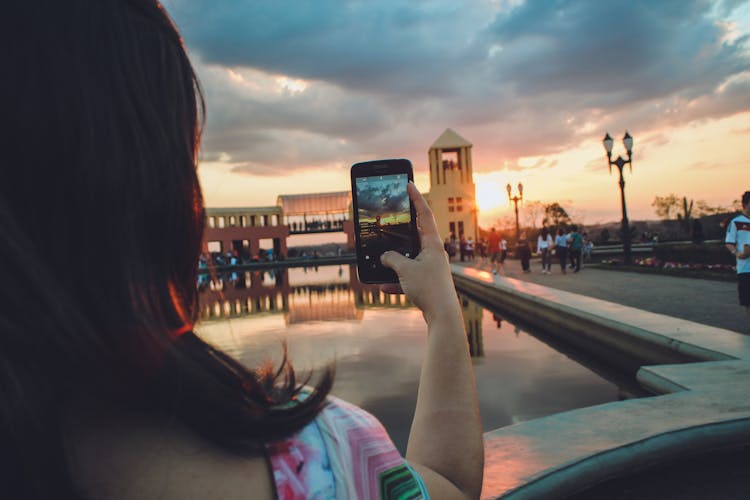 Woman Holding Smartphone Capturing Sunset