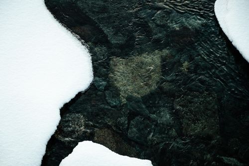 Free A serene winter stream flows over rocks, framed by untouched snow, capturing nature's tranquility. Stock Photo