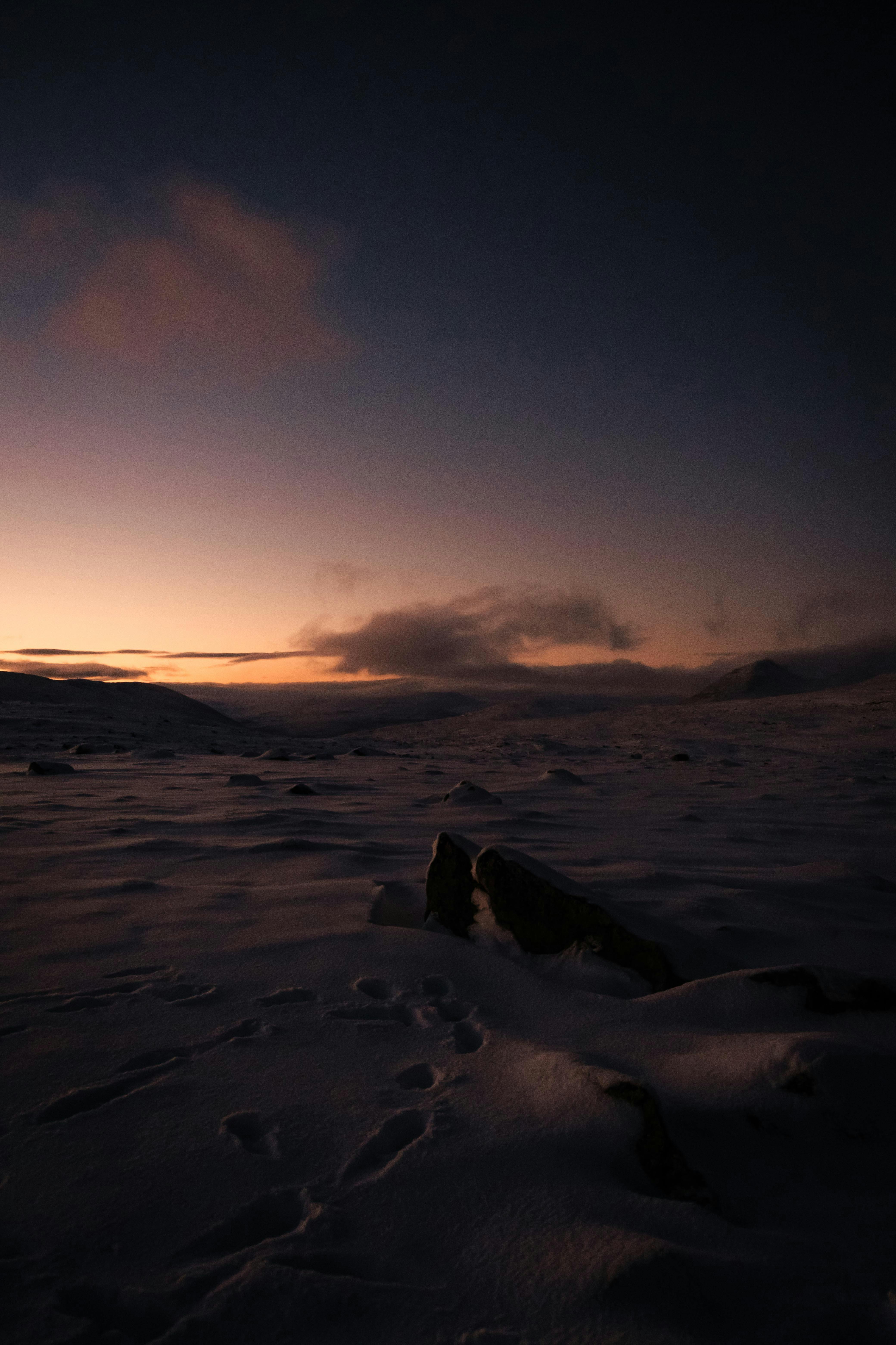 A serene winter sunset view over a snow-covered field with dramatic clouds in a tranquil landscape.