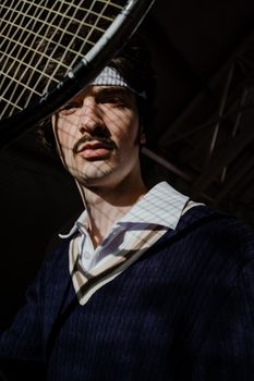 Portrait of a retro tennis player wearing a sweatband and holding a racket.