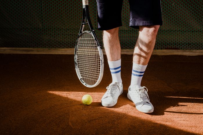 Ribbed white crew socks and court shoes on warm clay, racket resting alongside — photo by cottonbro studio on Pexels